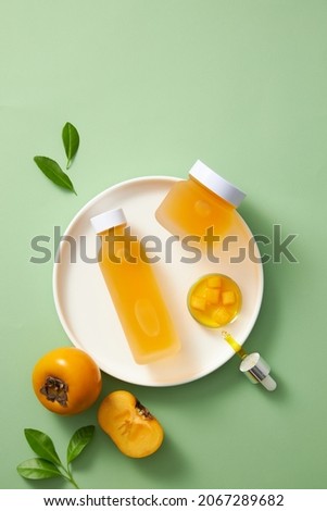 Persimmon extract bottle in a white dish with green leaf and green background  , cosmetic advertising , top view , petri dish