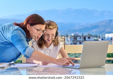 Child schoolgirl learning online with laptop, mom helping