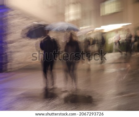 Abstract view of walking people holing umbrellas, on a street a rainy evening. Long shutter speed photography. Movement create imaginative motion blur.