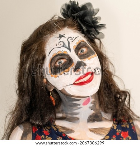 Image of a girl who poses with a skull mask make up on a gray background.