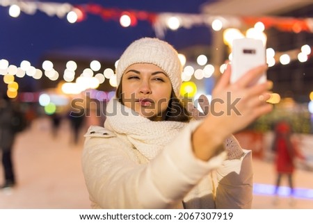 Happy young woman in winter on the ice rink taking picture on smartphone, selfie.