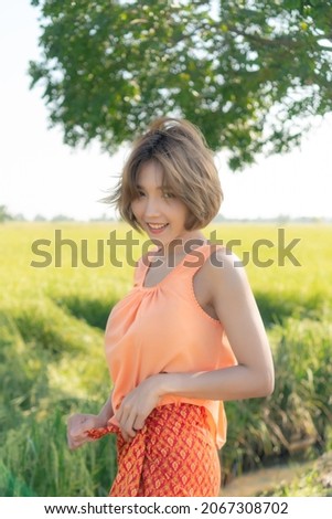 Asian woman. Wearing an orange shirt. Standing in a field.