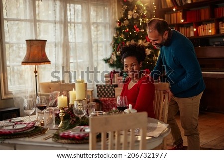 Romantic couple in love have dinner on on Christmas at home. Middle age caucasian man helping his beautiful black wife to sit at the dining table