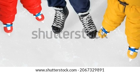 Close-up of the shoes of dad and  kids skating on ice rink. Banner with copy space for skating lessons and training. Two children in orange and red overalls next to a hockey coach. young athletes