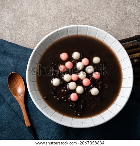 Top view of red and white tangyuan (tang yuan, glutinous rice dumpling balls) with sweet red bean soup in a bowl on gray table background for Winter solstice festival food. Royalty-Free Stock Photo #2067358634