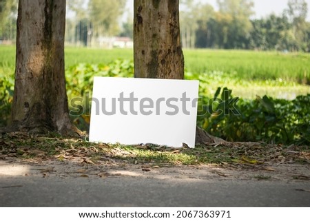 A blank white sign board leaning against a tree, Real shadow, and the background blur