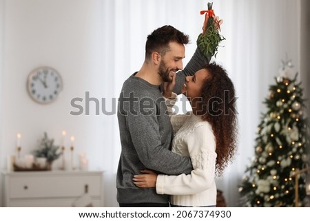 Lovely couple under mistletoe bunch in room decorated for Christmas