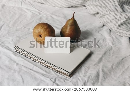 Couple of yellow pear fruit on blank notebook, diary. Business card mockup. Autumn, summer breakfast in bed composition.White striped linen bedding. Feminine lifestyle composition. Rustic interior. 