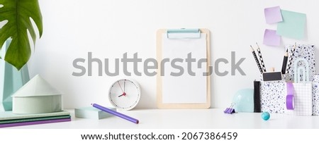 Desk in kids room with frame mock up, clock, books, notes on the wall and many purple supplies.
 Royalty-Free Stock Photo #2067386459