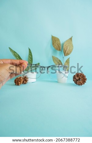 vertical photo. glasses, hands, pine flowers and green leaves on pink paper background. minimalist concept idea
