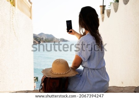 Young woman taking photo with phone near the sea. Happy woman enjoy in sunny day.	