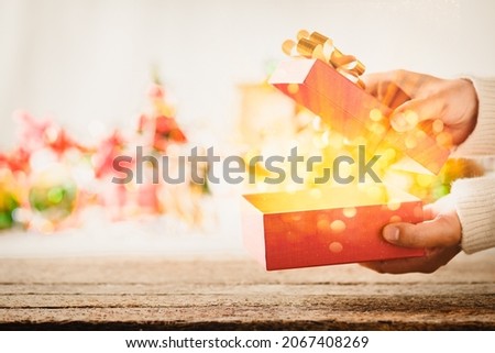 Open gift box with golden magic light coming out against Christmas lights background.
