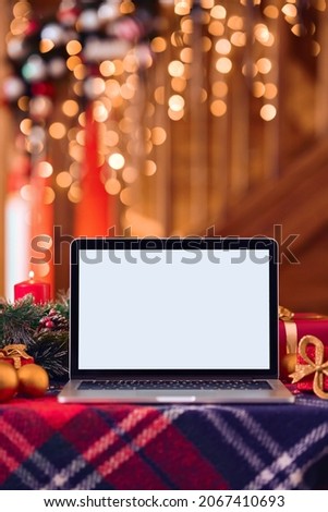 Laptop computer mockup white blank screen for ads on Christmas table holiday background. Xmas shopping online stores e commerce websites, virtual family party Happy New Year video calls, vertical.