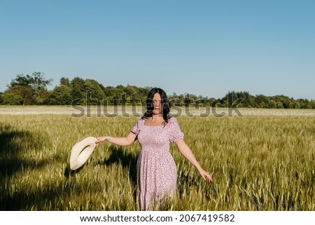 Lifestyle image of beautiful woman with long hair, walking in field and touching wheat or barley ears 