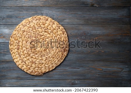 Wicker straw place mat on wooden dark background. Round woven straw mat on wooden gray dining table. Menu, dining, eating concept. Top view, copy space Royalty-Free Stock Photo #2067422390