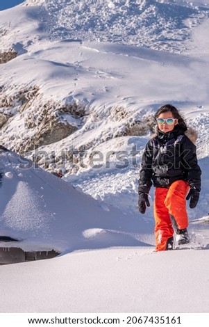 Child walking in snow. One Asian girl in ski-wear, sunglasses and gloves playing in winter. Happy childhood.