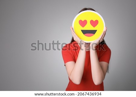 Woman covering face with heart eyes emoji on grey background, space for text Royalty-Free Stock Photo #2067436934