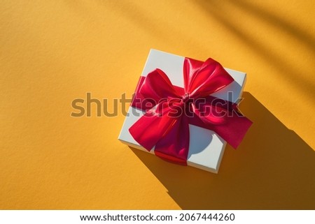White gift box with red ribbon on a yellow background. Valentines day backdrop. Flat lay style with minimalistic design. Template for banner or party invitation