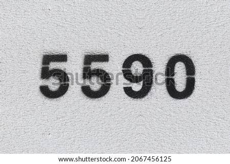 Black Number 5590 on the white wall. Spray paint. Number five thousand five hundred ninety.