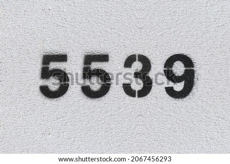 Black Number 5539 on the white wall. Spray paint. Number five thousand five hundred thirty nine.