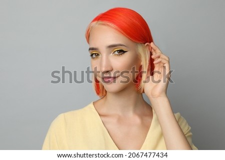 Beautiful young woman with bright dyed hair on light grey background