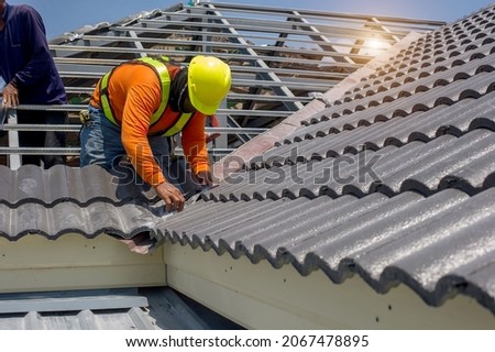 Roof repair, worker  replacing gray tiles or shingles on house with blue sky as background and copy space, Roofing - construction worker standing on a roof covering it with tiles. Royalty-Free Stock Photo #2067478895