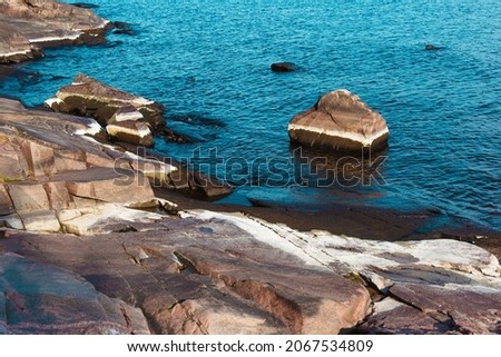 Rocky shore of Lake Ladoga on a sunny clear autumn day. Large smooth stones in blue water, horizontal banner