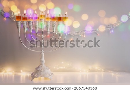 Image of jewish holiday Hanukkah with menorah (traditional candelabra) and oil candles over garland glitter lights background