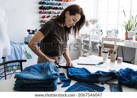 Denim Upcycling Ideas, Using Old Jeans, Repurposing Jeans, Reusing Old Jeans, Upcycle Stuff. Woman seamstress cut and repair old blue jeans in sewing studio. Royalty-Free Stock Photo #2067546047