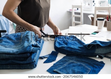 Denim Upcycling Ideas, Using Old Jeans, Repurposing Jeans, Reusing Old Jeans, Upcycle Stuff. Woman seamstress cut and repair old blue jeans in sewing studio. Royalty-Free Stock Photo #2067546050