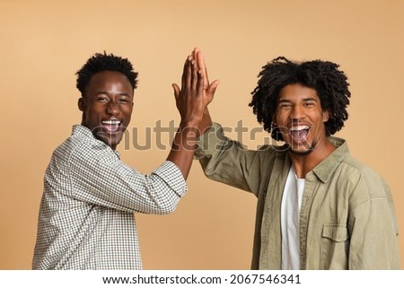 Two Cheerful Black Guys Giving High Five To Each Other, Positive Millennial African American Friends Celebrating Something, Laughing And Having Fun Together Over Beige Studio Background, Copy Space Royalty-Free Stock Photo #2067546341