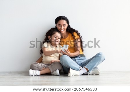 Online Shopping. Cute Little Girl And Her Mom Using Smartphone At Home, Happy Middle Eastern Mother And Preteen Daughter Relaxing On Floor With Mobile Phone, Enjoying Purchasing In Internet