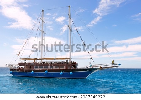 A pleasure sailboat plows the azure waters of the Red Sea, an imitation of a pirate ship, the sails are lowered, the blue sky with white cloud, pleasure motor boat, pleasure yacht