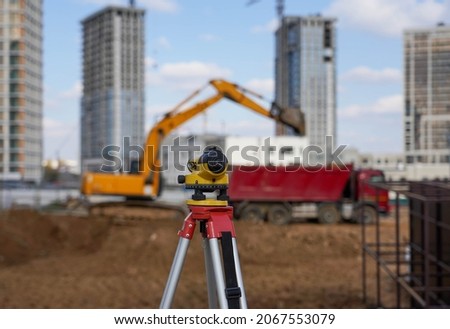 Photo of a level at the construction site of multi storey buildings with a yellow excavator and an red truck on the street in the city.