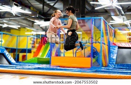 Pretty girls jumping together on colorful trampoline at playground park. Two sisters having fun during active entertaiments indoor Royalty-Free Stock Photo #2067553502