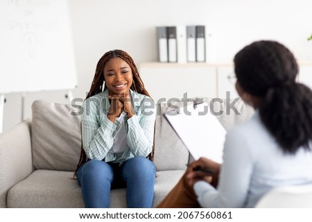 Successful psychotherapy. Millennial female client having session with psychologist, smiling, sitting on couch at clinic. Cheerful black lady communicating with therapist, solving emotional problem Royalty-Free Stock Photo #2067560861