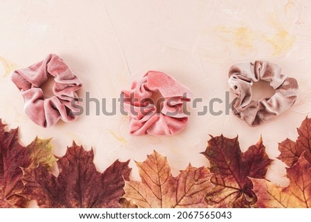 Pink and brown velvet scrunchies and autumn red and yellow maple leaves on pastel backround. Flat lay, top view. Diy accessories, hairstyle, lifestyle, outfit ideas for fall concept, copy space