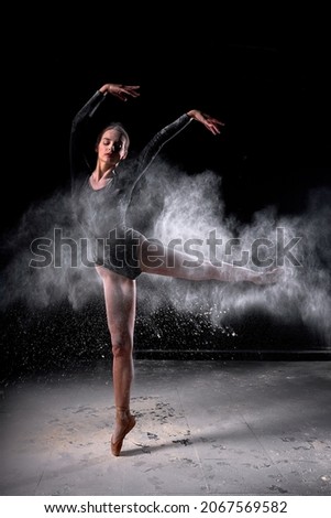 Dancer posing dancing gracefully in studio with cloud of dust, flour. Dancer in black bathing suit is moving, in action, having good choreographic training, raising leg up. ballet, dance, performance