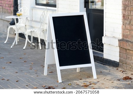 Signboard on the street. Empty menu board stand. Restaurant sidewalk chalkboard sign board. Freestanding A-frame blackboard near flower shop ur cafe. Copyspace for text, selective focus
