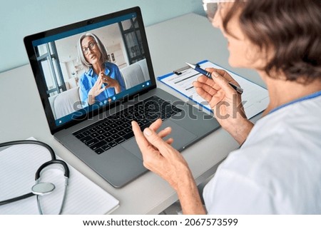Female doctor therapist consulting older senior patient via virtual video call visit using laptop computer. Digital online healthcare, distance telemedicine. Telehealth videocall. Over shoulder view Royalty-Free Stock Photo #2067573599