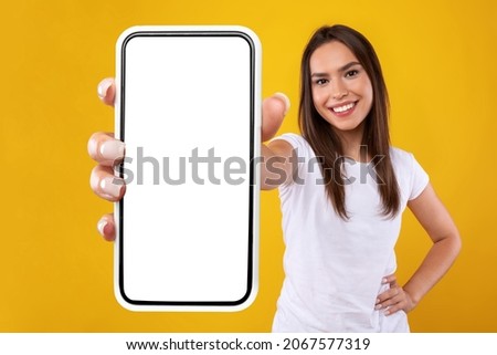 App Ad. Smiling pretty woman holding smartphone with white blank device screen in hand close up to camera, orange studio. Gadget with empty free space for mockup, banner isolated, selective focus Royalty-Free Stock Photo #2067577319