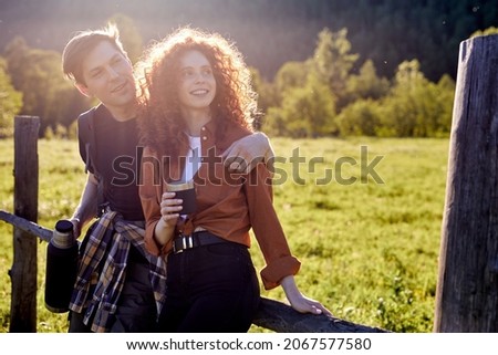 Man and woman spending time in nature together. Visiting countryside,active tourism. Hiking in the mountains vacation concept, have rest, drinking tea from thermos.Peaceful rural environment.