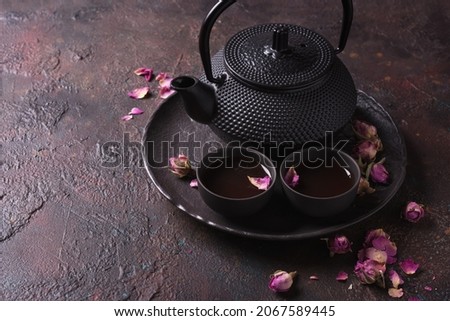 Japanese black cast iron teapot and herbal tea with dried rose buds on dark concrete background