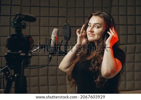 Young girl with microphone and headphones in recording studio. Recording of vocal, blogger, reading text, voice acting.