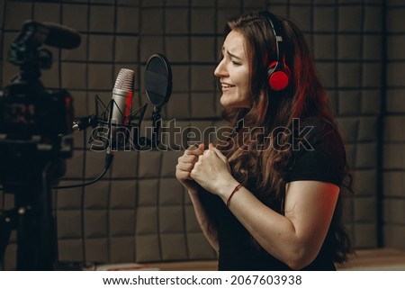 Young girl with microphone and headphones in recording studio. Recording of vocal, blogger, reading text, voice acting.