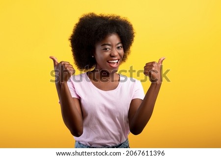 Best choice. Happy african american lady showing thumbs up gesture with both hands, approving or recommending something good, posing isolated on yellow studio wall, banner Royalty-Free Stock Photo #2067611396