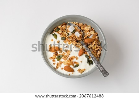 Top view of the traditional morning dish granola with almonds, pumpkin seeds, coconut, dried oat flakes and other cereals with yogurt in a gray bowl with a spoon Royalty-Free Stock Photo #2067612488