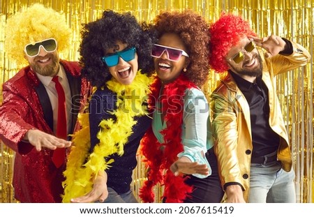 Bunch of excited young friends having fun together. Diverse group of happy people in boas, cool sunglasses and funny silly curly wigs dancing at crazy pop music nightclub disco party Royalty-Free Stock Photo #2067615419