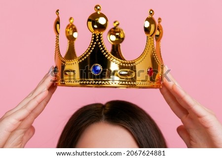 Unknown woman putting on golden crown, arrogance and privileged status, concept of self confidence in success, self-motivation and dreams to be best. Indoor studio shot isolated on pink background. Royalty-Free Stock Photo #2067624881