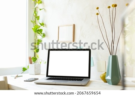 Stylish home office desk with laptop mock up, office supplies, frame, vase, green ivy and beige natural texture wall. Distance working and learning concept. Trendy, creative workspace.